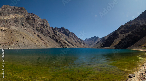 The deep blue color water lake very high in the Andes mountains. Panorama view of the Inca Lagoon in Chile, surrounded by rocky mountains in a summer sunny day.