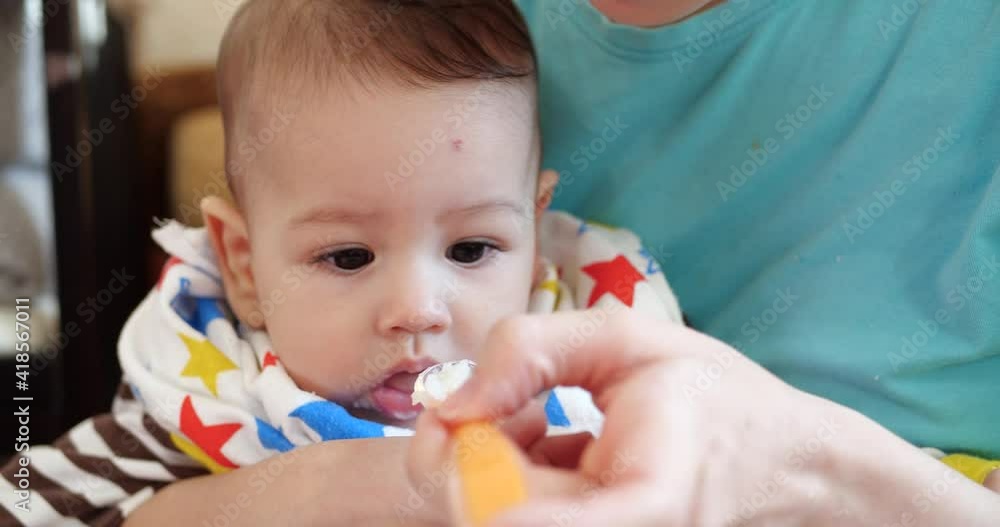 mother holds the baby in her arms and feeds her boy with a spoon. family, food, child, eating and parenthood concept. slow motion mother holds the baby in her arms and feeds her boy with a spoon. family, food, child, eating and parenthood concept. slow motion