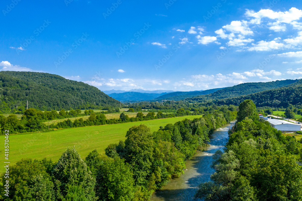 Aerial view from drone of the vast green landscape with river, hills and blue sky