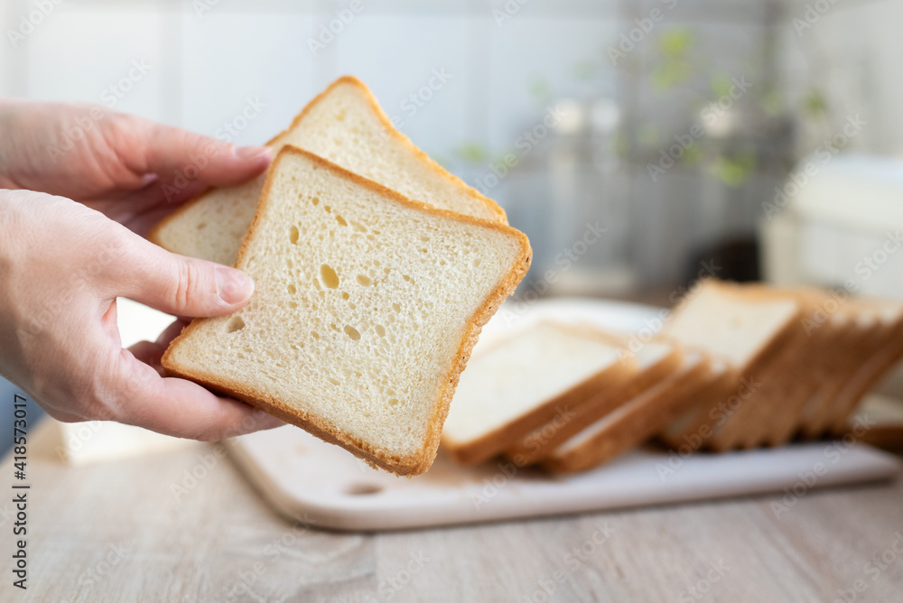 Female hands holding two slices of white bread on the background of the kitchen.