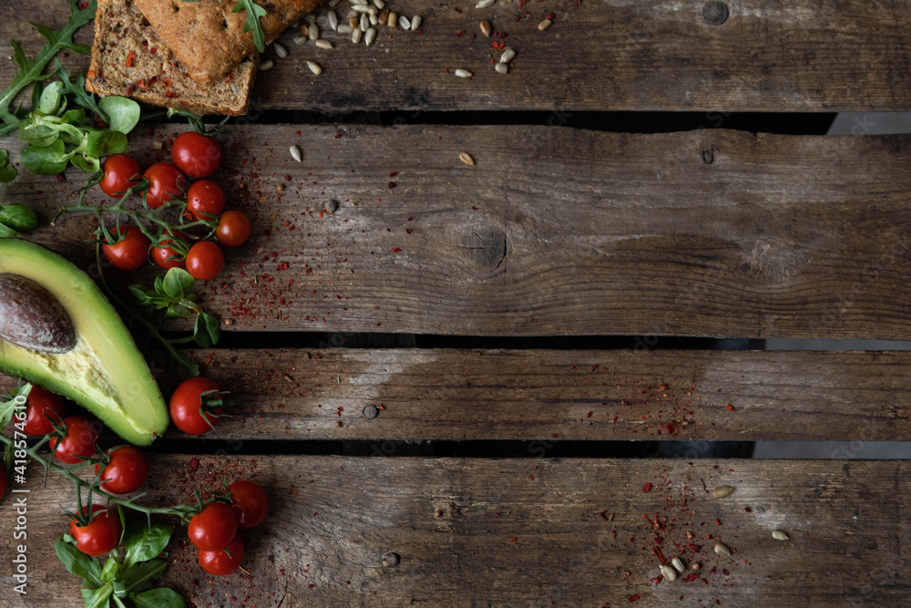 Copy space. On a wooden background, on the left, cherry tomatoes, avocado, garlic bun, herbs and sunflower seeds are laid out with vegetables. Rustic style of healthy eating