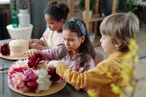 Group of kids putting handmade flowers of white, pink and crimson colors on hat