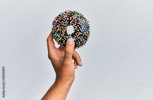 Hand of hispanic man holding chocolate donut over isolated white background.