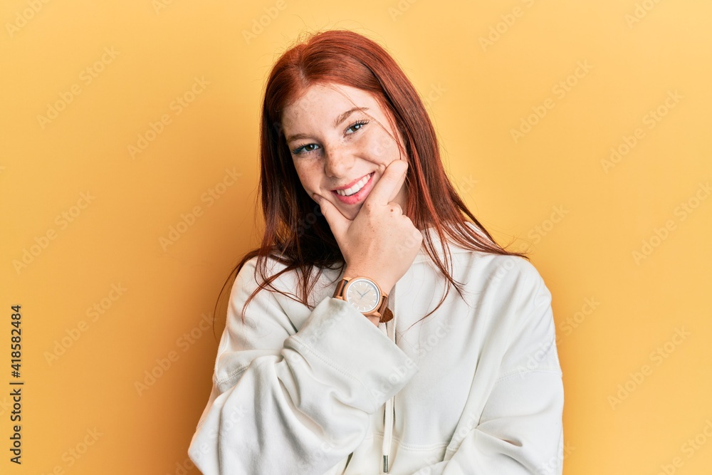 Young red head girl wearing casual sweatshirt looking confident at the camera smiling with crossed arms and hand raised on chin. thinking positive.