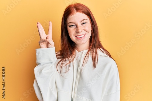 Young red head girl wearing casual sweatshirt showing and pointing up with fingers number three while smiling confident and happy.