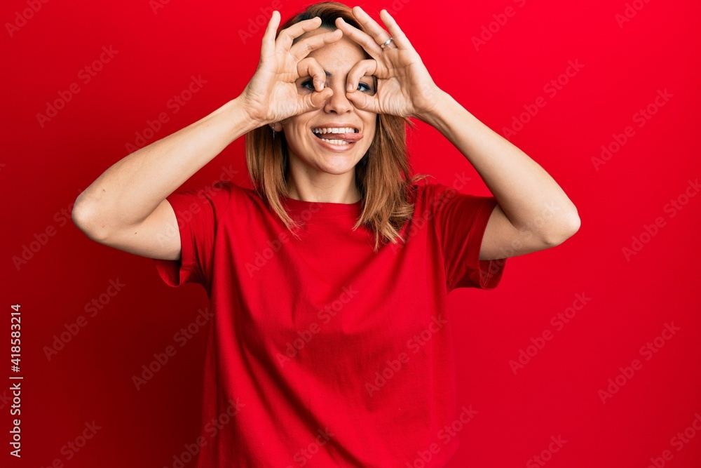 Hispanic young woman wearing casual red t shirt doing ok gesture like binoculars sticking tongue out, eyes looking through fingers. crazy expression. Hispanic young woman wearing casual red t shirt doing ok gesture like binoculars sticking tongue out, eyes looking through fingers. crazy expression.