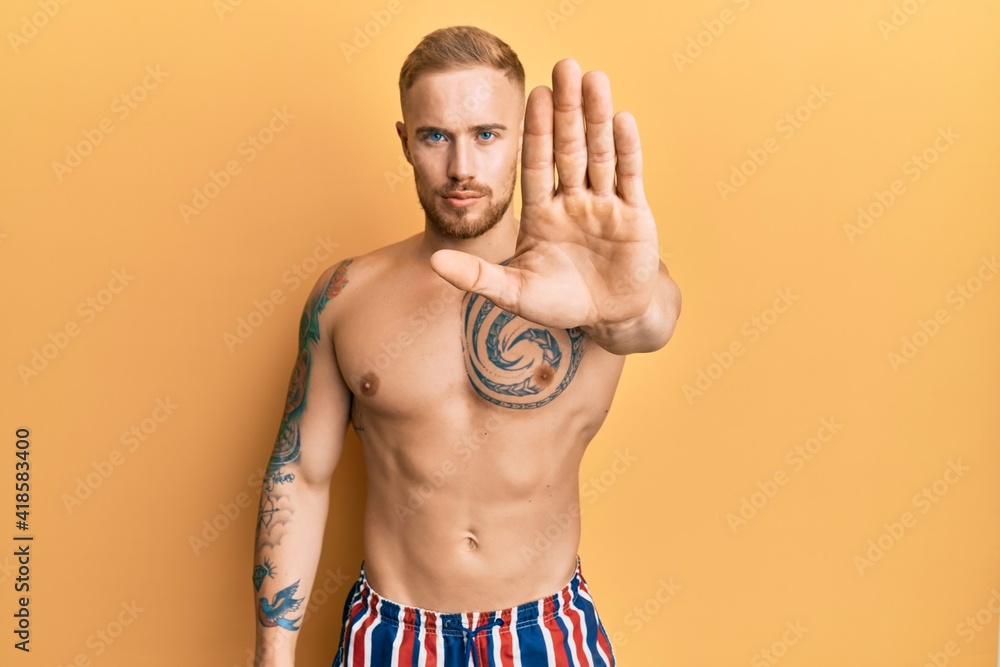 Young caucasian man wearing swimwear shirtless doing stop sing with palm of the hand. warning expression with negative and serious gesture on the face.