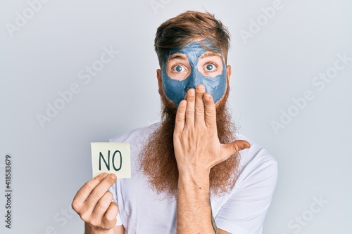 Young irish redhead man wearing facial mask holding no reminder covering mouth with hand, shocked and afraid for mistake. surprised expression