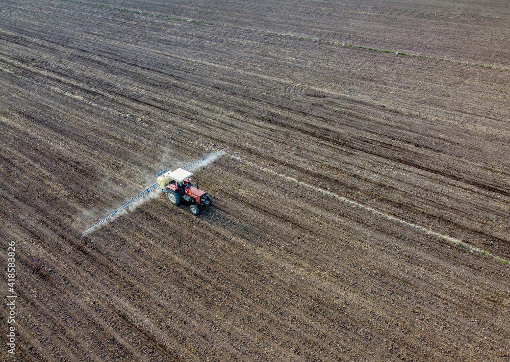 Aerial view of a farm machine sprays a green wheat field at sunset.