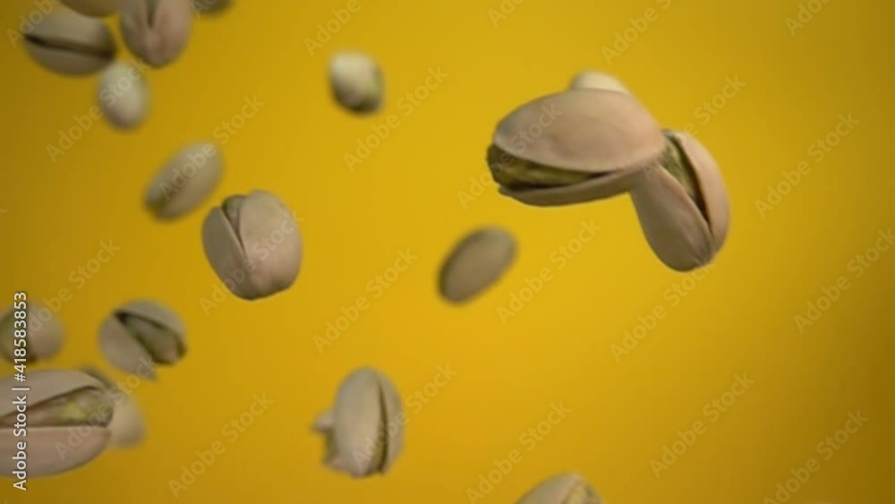 Close-up of salted pistachios falling on a yellow background in slow motion Close-up of salted pistachios falling on a yellow background in slow motion