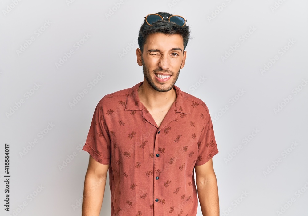 Young handsome man wearing casual summer clothes winking looking at the camera with sexy expression, cheerful and happy face. Young handsome man wearing casual summer clothes winking looking at the camera with sexy expression, cheerful and happy face.