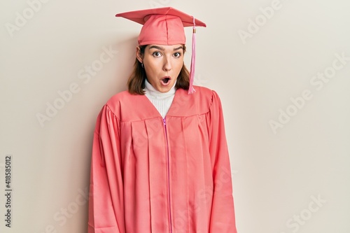 Young caucasian woman wearing graduation cap and ceremony robe afraid and shocked with surprise expression, fear and excited face.