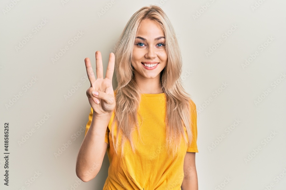 Beautiful caucasian blonde girl wearing casual tshirt showing and pointing up with fingers number three while smiling confident and happy. - obrazy, fototapety, plakaty 
