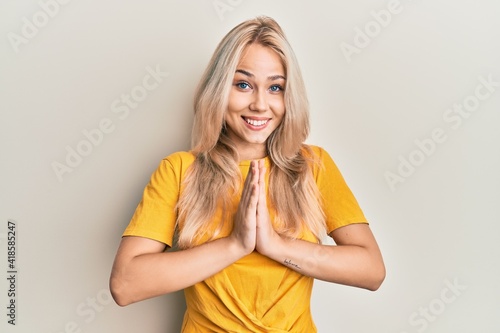 Beautiful caucasian blonde girl wearing casual tshirt praying with hands together asking for forgiveness smiling confident.