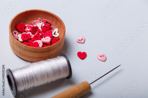 wooden bowl of heart shaped red and pink buttons with spool of threads and awl for sewing and embroidery on white background. Set of materials for handcraft, making of bijouterie and accessories photo