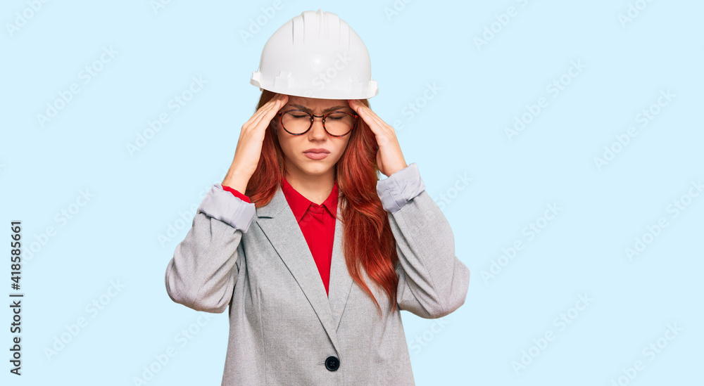 Young redhead woman wearing architect hardhat with hand on head for pain in head because stress. suffering migraine. Young redhead woman wearing architect hardhat with hand on head for pain in head because stress. suffering migraine.