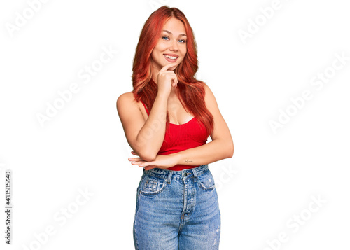 Bilde på lerret Young redhead woman wearing casual clothes looking confident at the camera with smile with crossed arms and hand raised on chin