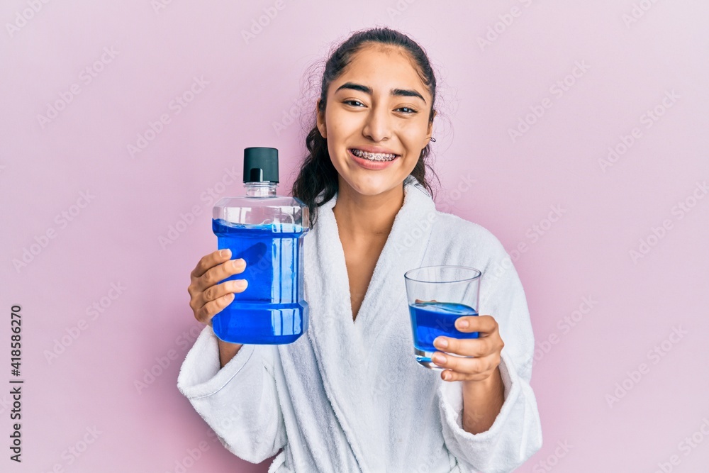 Hispanic teenager girl with dental braces holding mouthwash smiling with a happy and cool smile on face. showing teeth. Hispanic teenager girl with dental braces holding mouthwash smiling with a happy and cool smile on face. showing teeth.
