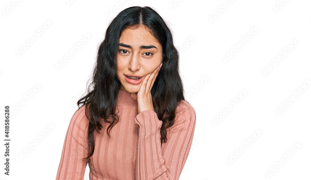 Hispanic teenager girl with dental braces wearing casual clothes touching mouth with hand with painful expression because of toothache or dental illness on teeth. dentist Hispanic teenager girl with dental braces wearing casual clothes touching mouth with hand with painful expression because of toothache or dental illness on teeth. dentist