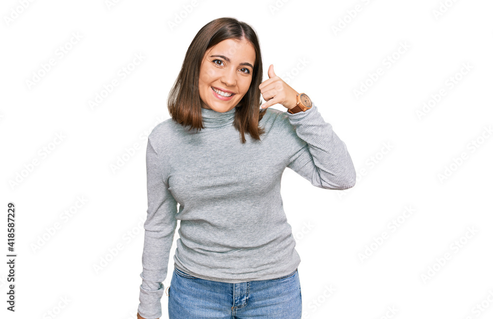 Young beautiful woman wearing casual turtleneck sweater smiling doing phone gesture with hand and fingers like talking on the telephone. communicating concepts. Young beautiful woman wearing casual turtleneck sweater smiling doing phone gesture with hand and fingers like talking on the telephone. communicating concepts.