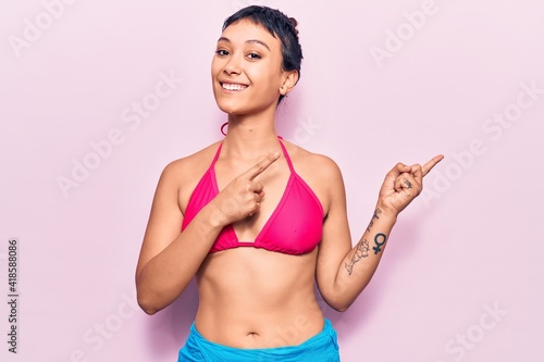 Young woman wearing bikini smiling and looking at the camera pointing with two hands and fingers to the side. © Krakenimages.com