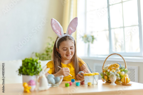 Cute little child wearing bunny ears painting eggs.