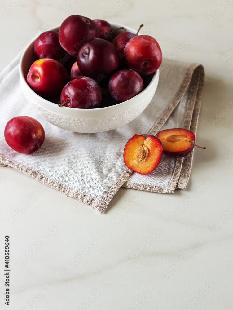 Ripe red plums in a white plate on marble background. Healthy food. Ripe red plums in a white plate on marble background. Healthy food.