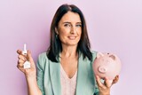 Middle age brunette woman holding house keys and piggy bank smiling with a happy and cool smile on face. showing teeth.