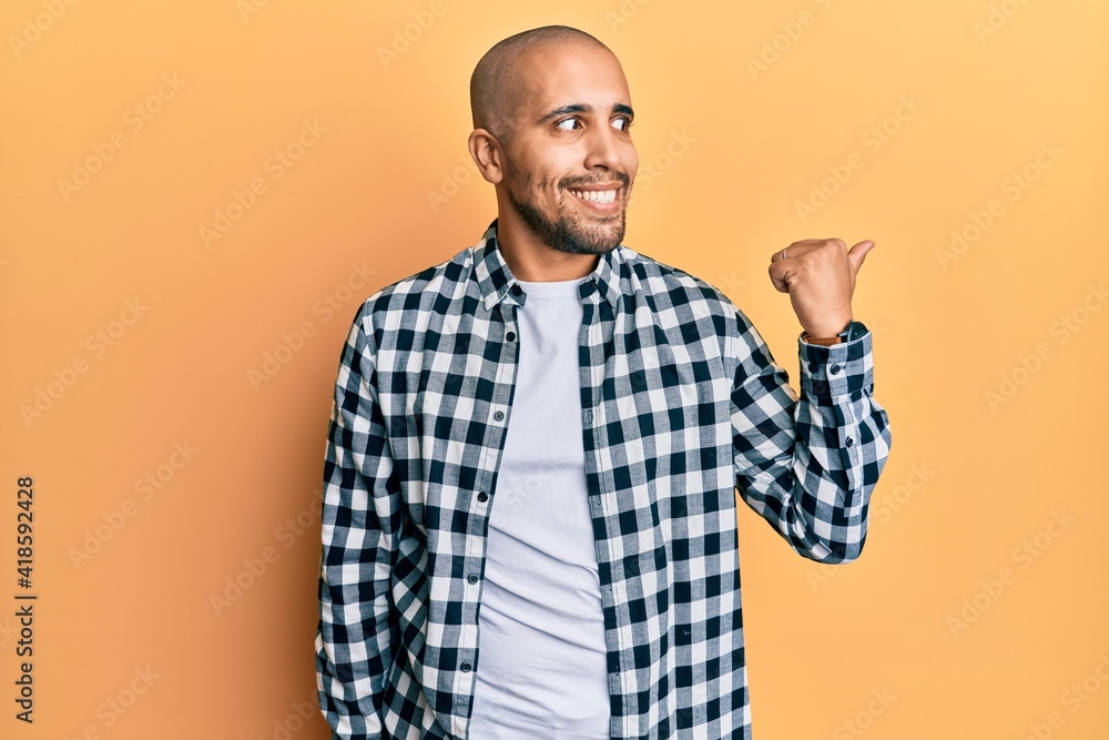 Hispanic adult man wearing casual clothes pointing thumb up to the side smiling happy with open mouth Hispanic adult man wearing casual clothes pointing thumb up to the side smiling happy with open mouth