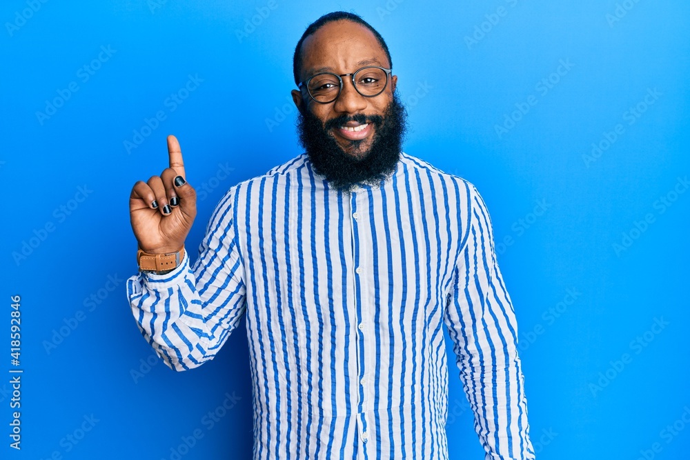 Naklejka premium Young african american man wearing business style smiling with an idea or question pointing finger up with happy face, number one