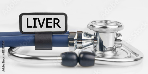 On the white surface lies a stethoscope with a plate with the inscription - LIVER