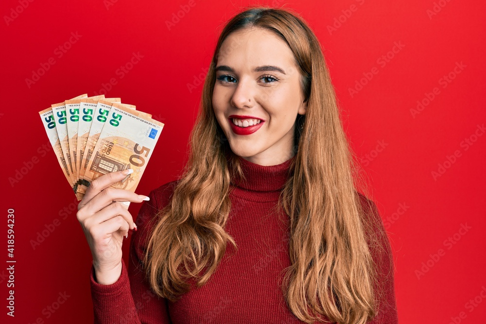 Young blonde woman holding euro banknotes looking positive and happy standing and smiling with a confident smile showing teeth Young blonde woman holding euro banknotes looking positive and happy standing and smiling with a confident smile showing teeth