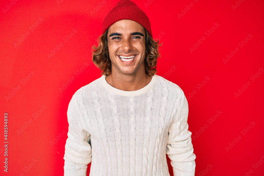 Young hispanic man wearing wool sweater and winter hat looking positive and happy standing and smiling with a confident smile showing teeth Young hispanic man wearing wool sweater and winter hat looking positive and happy standing and smiling with a confident smile showing teeth