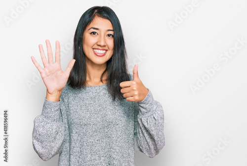 Beautiful asian young woman wearing casual clothes showing and pointing up with fingers number six while smiling confident and happy.