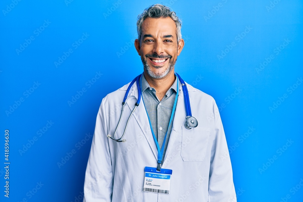 Middle age grey-haired man wearing doctor uniform and stethoscope with a happy and cool smile on face. lucky person. Middle age grey-haired man wearing doctor uniform and stethoscope with a happy and cool smile on face. lucky person.