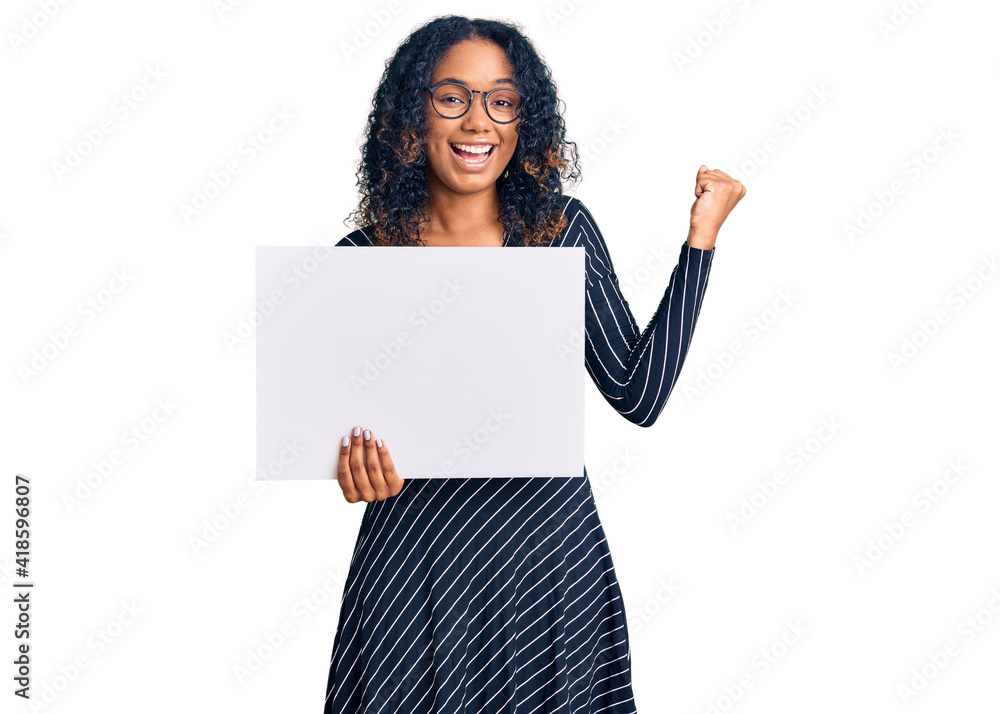 Young african american woman holding blank empty banner screaming proud, celebrating victory and success very excited with raised arms Young african american woman holding blank empty banner screaming proud, celebrating victory and success very excited with raised arms