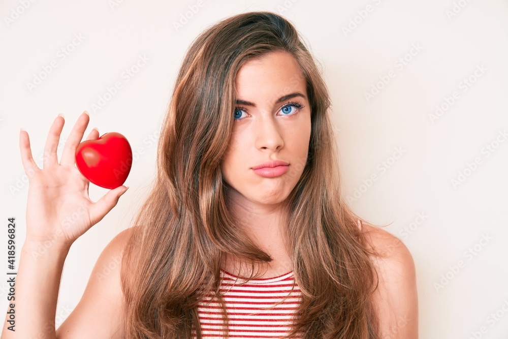 Beautiful young caucasian woman holding heart thinking attitude and sober expression looking self confident