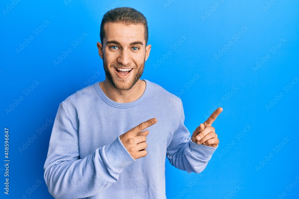 Young caucasian man pointing with fingers to the side smiling and laughing hard out loud because funny crazy joke. Young caucasian man pointing with fingers to the side smiling and laughing hard out loud because funny crazy joke.