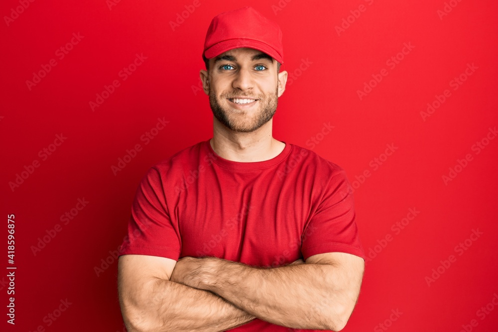Young caucasian man wearing delivery uniform and cap happy face smiling with crossed arms looking at the camera. positive person. Young caucasian man wearing delivery uniform and cap happy face smiling with crossed arms looking at the camera. positive person.