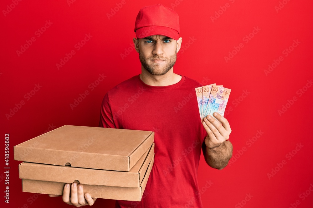 Young caucasian man holding delivery box and swiss franc banknotes skeptic and nervous, frowning upset because of problem. negative person. Young caucasian man holding delivery box and swiss franc banknotes skeptic and nervous, frowning upset because of problem. negative person.