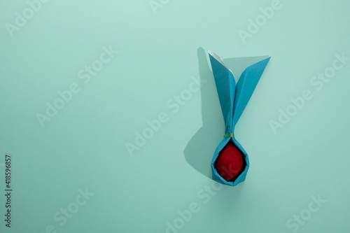 An red Easter egg in a green rabbit-shaped napkin. Flat lay on mint background.