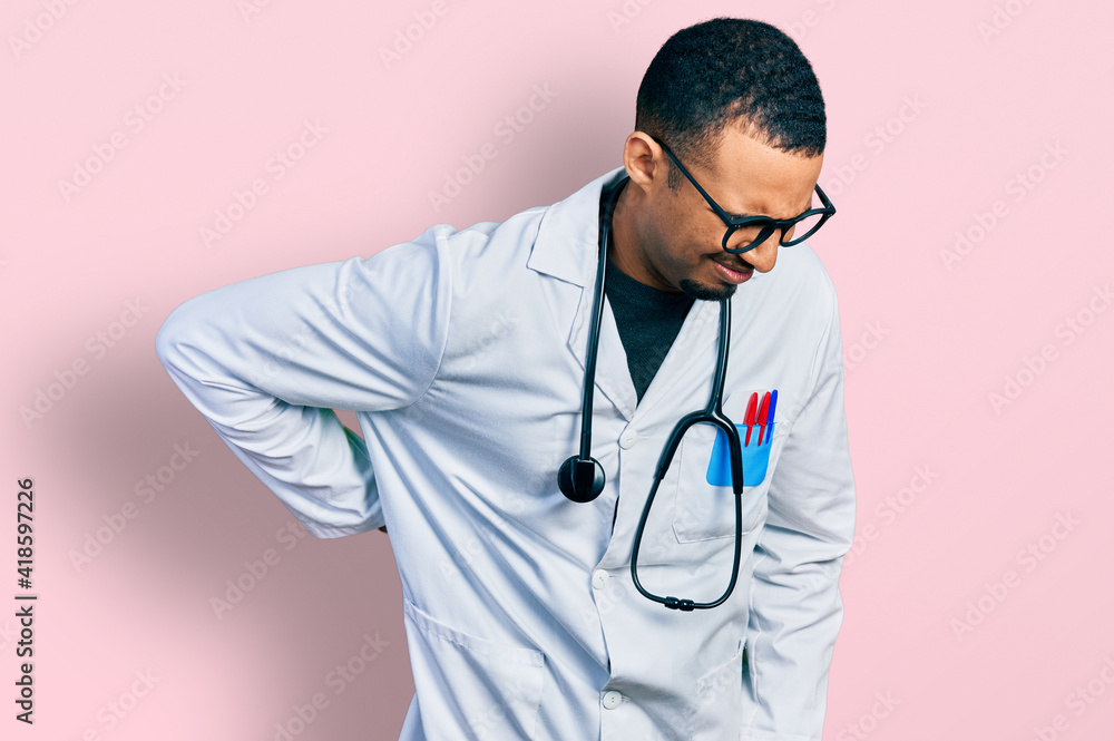 Young african american man wearing doctor uniform and stethoscope suffering of backache, touching back with hand, muscular pain Young african american man wearing doctor uniform and stethoscope suffering of backache, touching back with hand, muscular pain