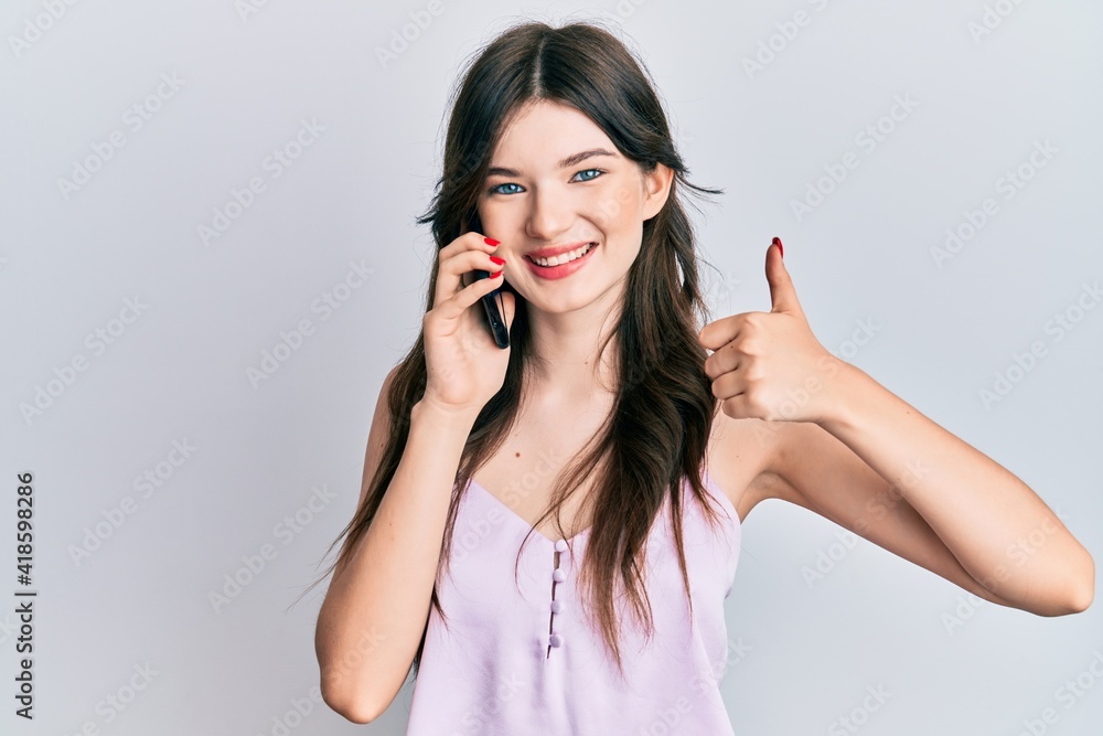 Young beautiful caucasian girl having conversation talking on the smartphone smiling happy and positive, thumb up doing excellent and approval sign Young beautiful caucasian girl having conversation talking on the smartphone smiling happy and positive, thumb up doing excellent and approval sign