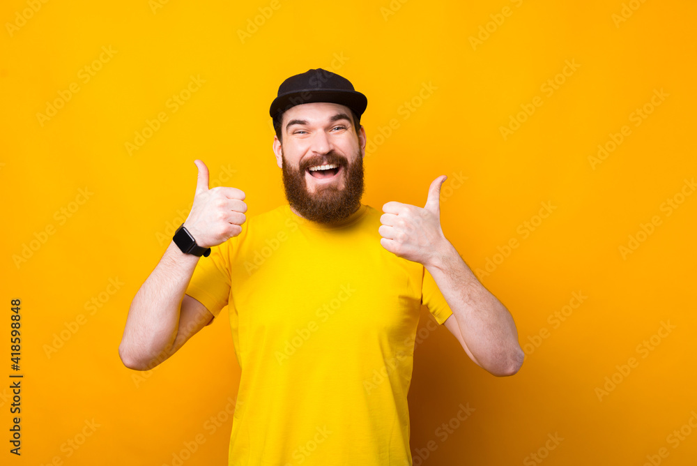 Fototapeta premium Amazed bearded hipster man showing thumbs up gesture over yellow background