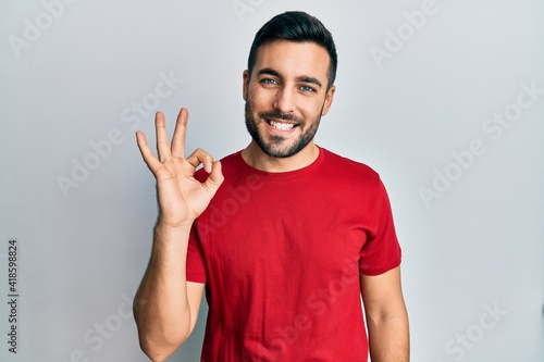 Young hispanic man wearing casual clothes smiling positive doing ok sign with hand and fingers. successful expression.