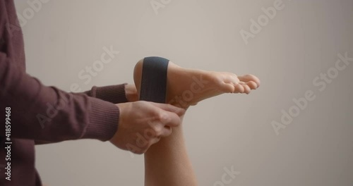 Physiotherapist sticks kinesio tapes to the heel of female patient, kinesiology taping, kinesiological therapy, athlete are recovering after injury, 4k 60p Prores HQ 10 bit photo