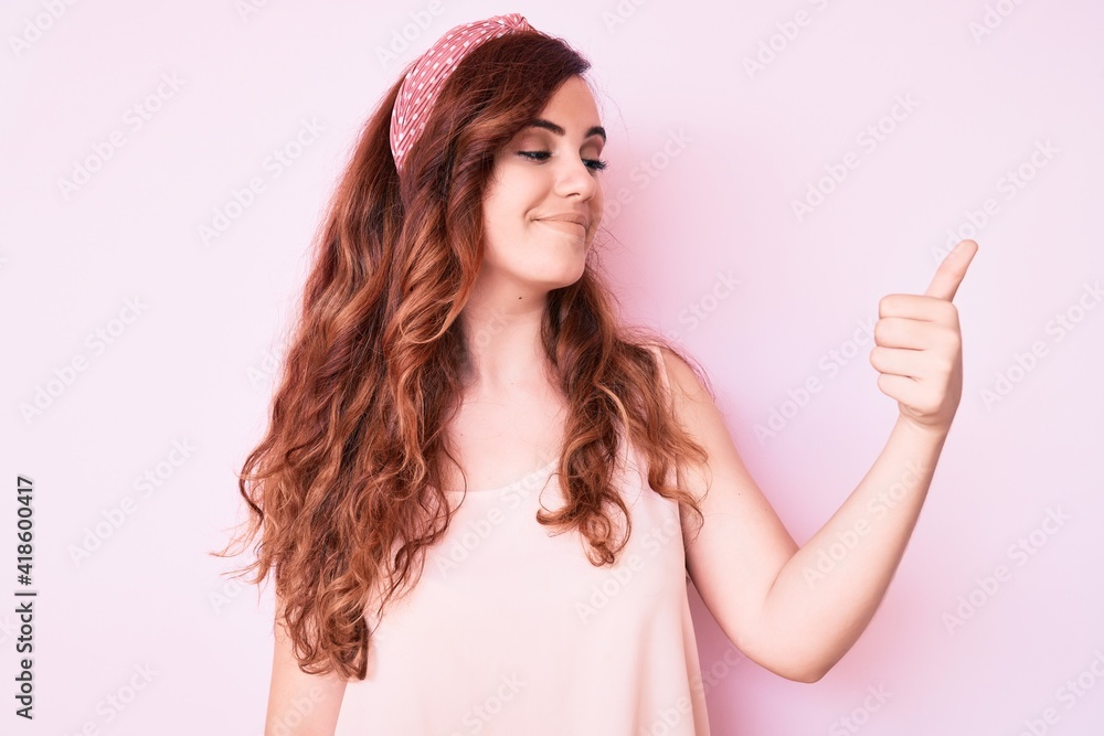 Young beautiful woman wearing casual clothes looking proud, smiling doing thumbs up gesture to the side Young beautiful woman wearing casual clothes looking proud, smiling doing thumbs up gesture to the side