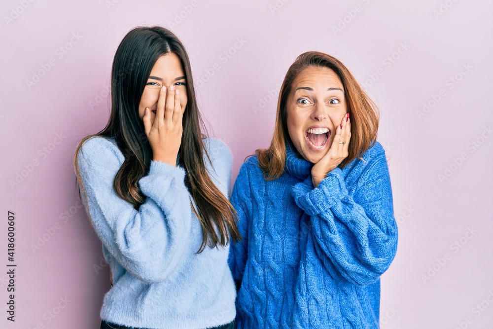 Hispanic family of mother and daughter wearing wool winter sweater laughing and embarrassed giggle covering mouth with hands, gossip and scandal concept Hispanic family of mother and daughter wearing wool winter sweater laughing and embarrassed giggle covering mouth with hands, gossip and scandal concept