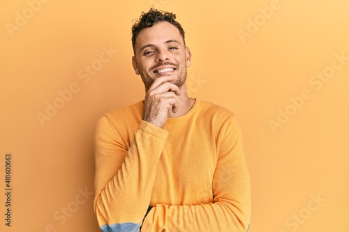 Young hispanic man wearing casual clothes smiling looking confident at the camera with crossed arms and hand on chin. thinking positive. © Krakenimages.com