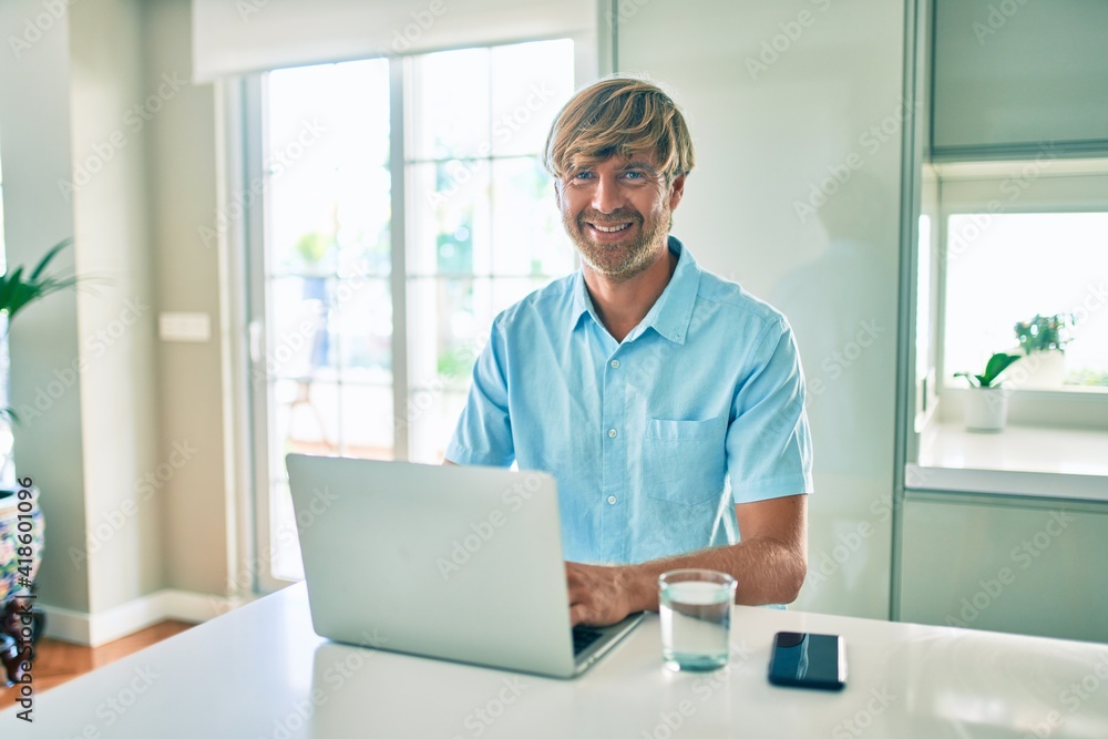 Young irish man smiling happy working using laptop sitting on the table at home. Young irish man smiling happy working using laptop sitting on the table at home.